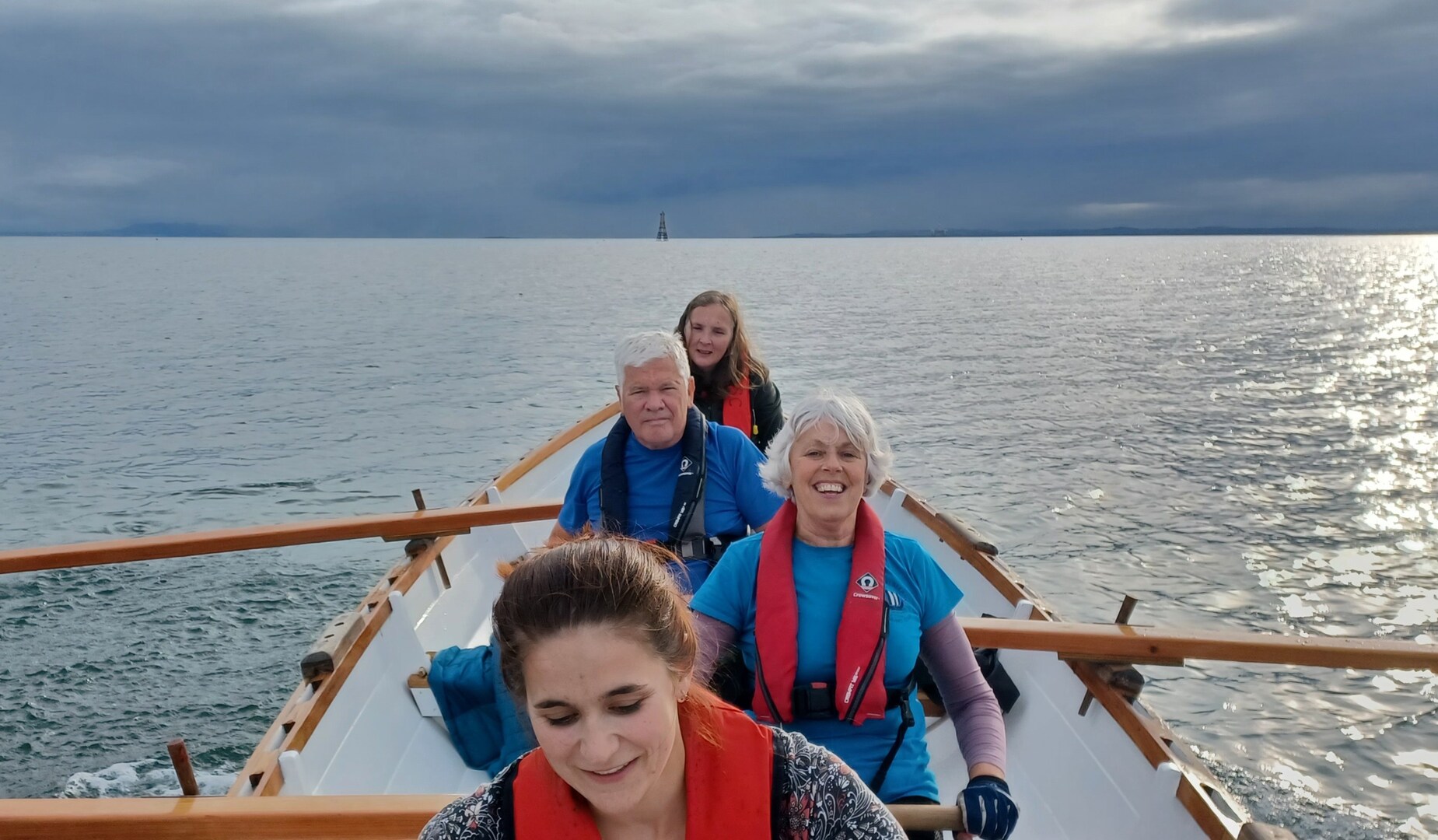 Four people rowing a boat on the water.