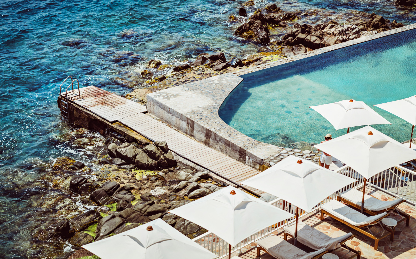 Hotel pool and lounge area next to the ocean.