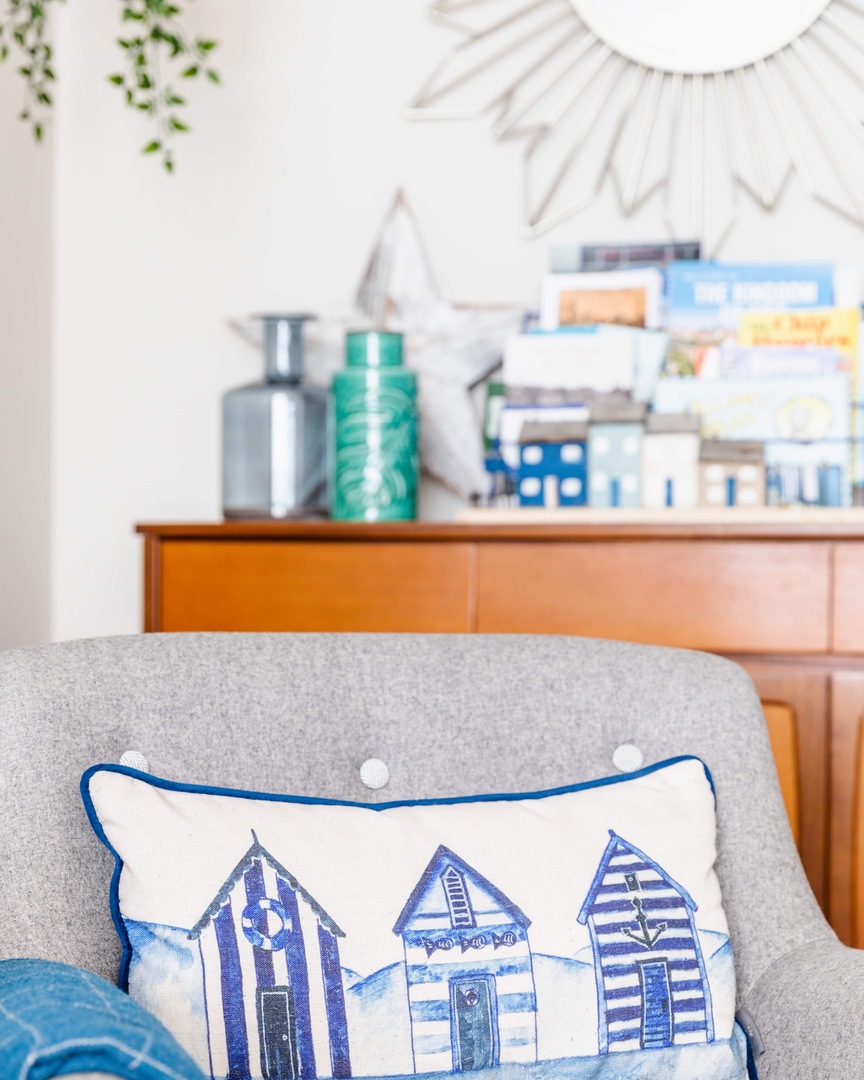 Pillow with beach hut illustration on a grey chair.