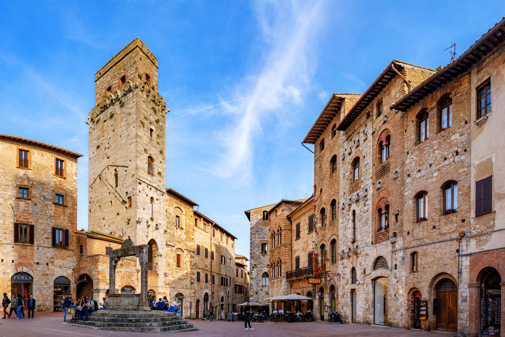 Historic square dominated by medieval buildings and a tall stone tower in San Gimignano, Tuscany.